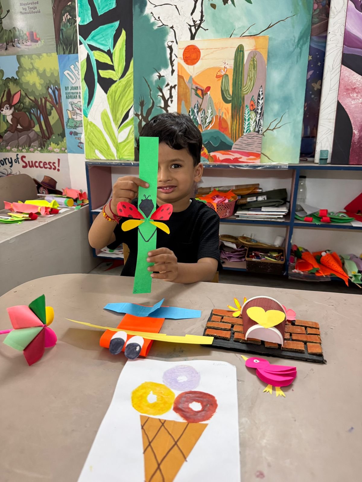 A boy showing his paper craft ladybug and airplane creations