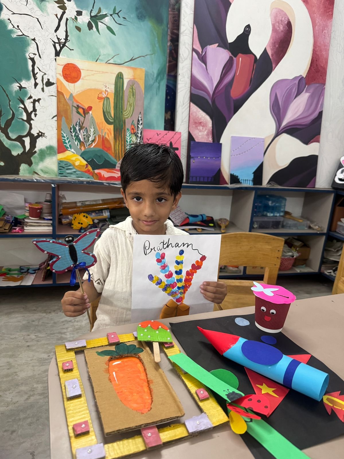 A boy holding his colourful handprint painting alongside craft projects