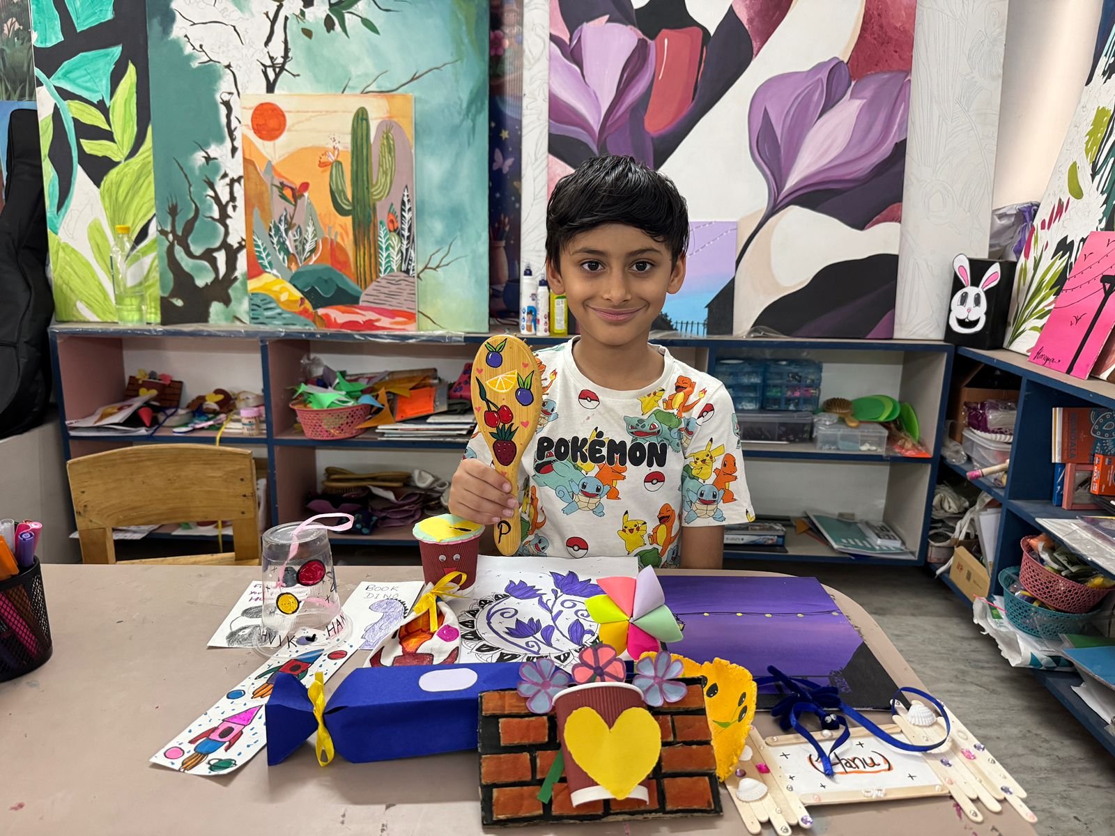 A boy holding a hand-painted wooden spoon and other craft creations
