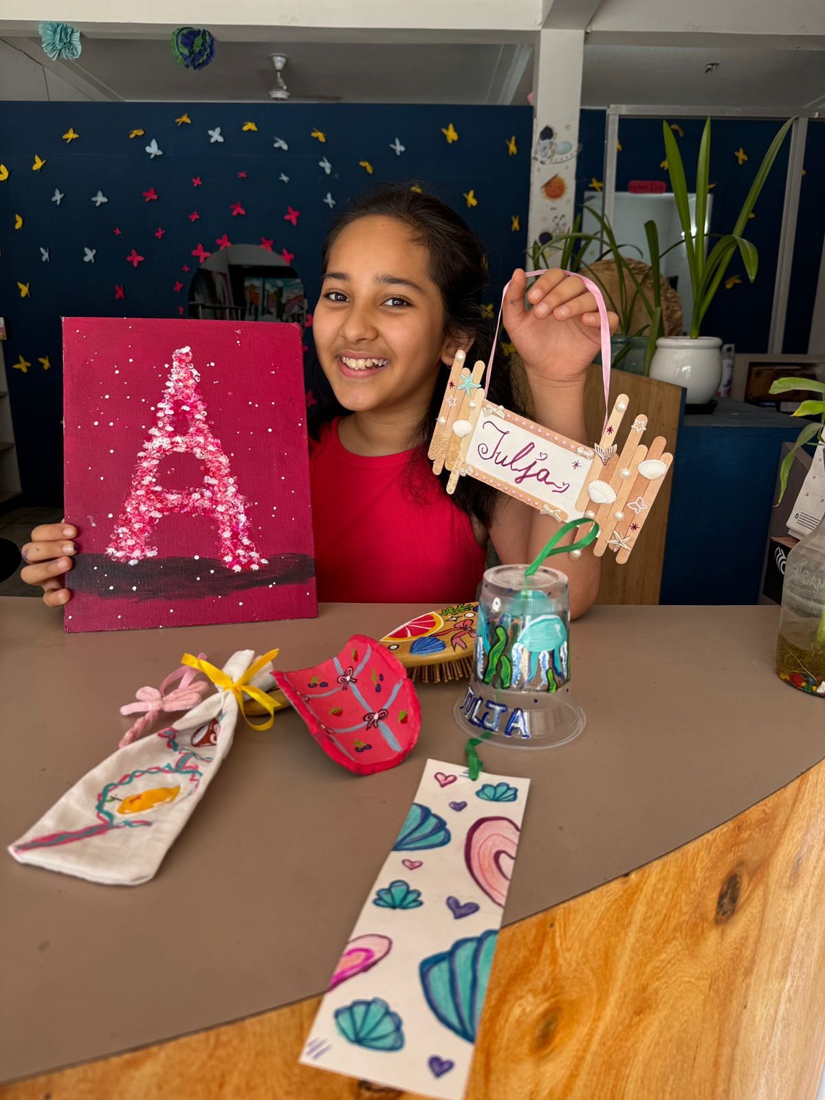 A girl holding her glitter letter painting and a handmade name plaque
