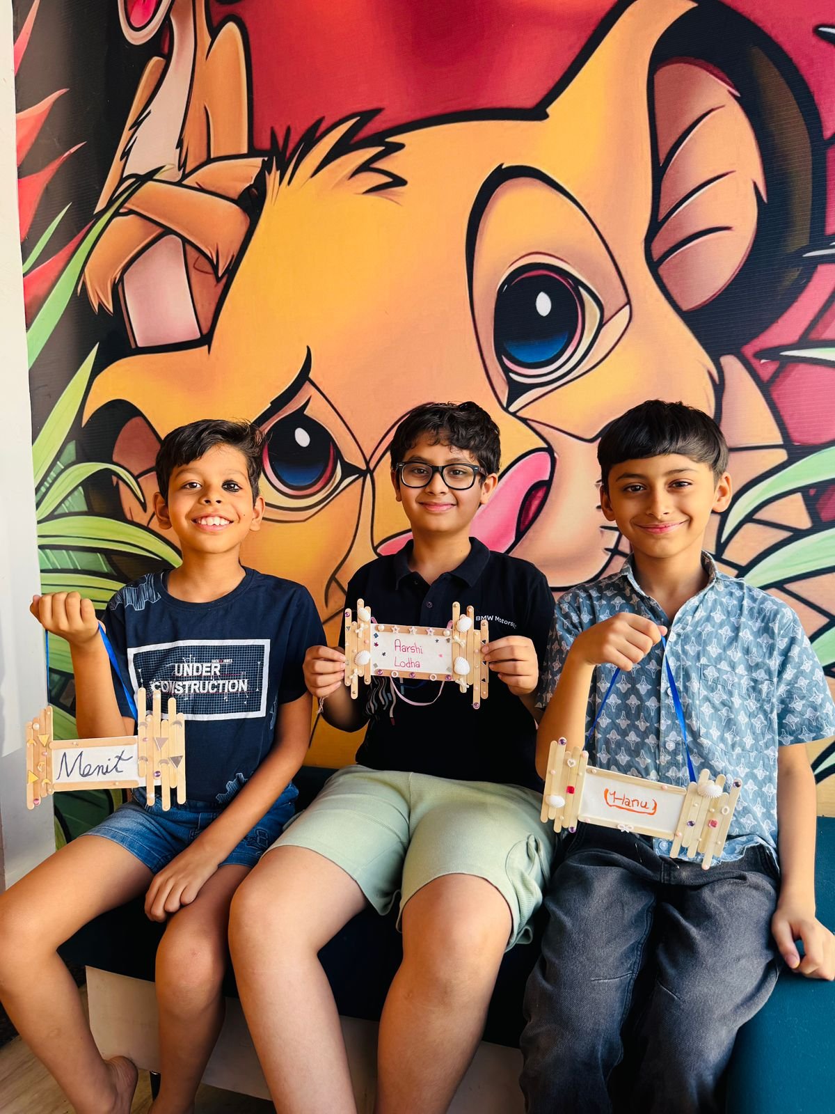 Three boys holding their handmade name plaques made from popsicle sticks